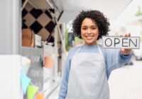 woman standing in front of food truck holding a sign that says open