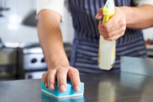 employee cleaning kitchen counter with sponge and cleaner